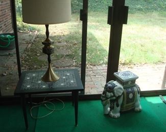 Sun Room:  A mid-century brass lamp (a closer photo follows) rests on a mid-century tile top table.  To the right is a ceramic elephant garden bench.