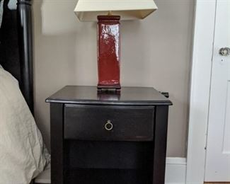 One of a pair of black wood beside tables and oxblood glazed terra cotta table lamps.