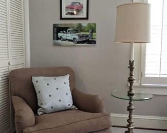 Large, comfy, upholstered armchair, with very handsome floor lamp, with round glass . Above, three of mans favorite things, vintage trucks and nude women.