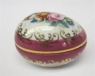 A 2 1/8" wide porcelain trinket box in the form of an egg. Marked limoge France. Transfer image of blossoms on the lid