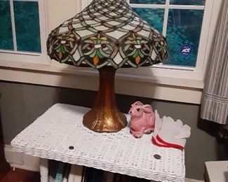 Wicker end table with book storage. Table top lamp with stained glass lampshade. Small figurines and decor. Books.