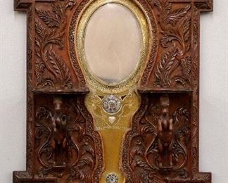 A late 18th/Early 19th century Indian "Aranmula Kannadi" Brass and Silvered hand mirror.  A highly polished metal mirror in an engraved Brass frame with Silver mounts.  In a later late 19th century carved Rosewood frame with two shaped candle shelves and horse form supports and deeply carved floriform decoration and deities in the corner reserves. Old finish with minor wear, one horse lacks fore leg.  15 1/2 x 20 1/2" overall.  ESTIMATE $300-500