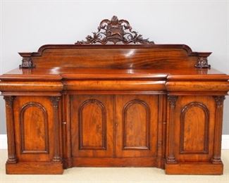 An early 19th century English William IV Period Mahogany sideboard.  Mahogany with Crotch Mahogany panels and Pine secondary wood.  Features a shaped backboard with carved crest over a molded inverted breakfront form top with three silverware drawers in the frieze, on a conforming base with two central doors with arched, molded panels flanked by end doors with arched molded panels and attached fluted columns and carved foliate capitols, one end with fitted bottle drawer.  Re-polished with minor wear, some old repair.  89 x 26 1/2 x 63" high overall.  ESTIMATE $2,000-4,000