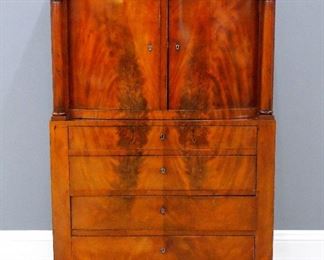 An early 19th century Biedermeier Period linen cabinet, Denmark or Northern German origin.  Mahogany construction with Crotch Mahogany veneer and Pine secondary wood.  Features a stepped top over two bowed doors flanked by turned columns and carved foliate capitols, on a plinth base with four graduated drawers.  Re-polished with good color, slight wear, some shrinkage cracks and minor edge damage.  42 x 20 1/2 x 63" high.  ESTIMATE $1,000-1,500