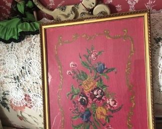 A large needlepoint, which frames an old cat toy and a doll, not to mention the  lace piece