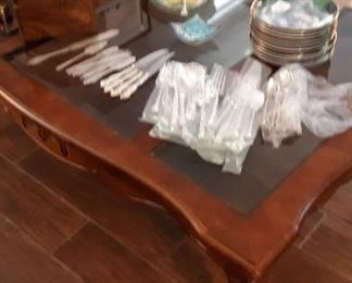 Glass and wood coffee table with silver plate flatware plates and decorating  items