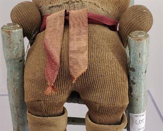 Antique well loved bear in corduroy and sitting in small wooden chair.