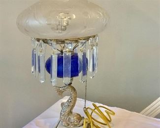 $295 - Lamp with cobalt blue body, metallic dolphin base, and intact prisms with removable etched frosted glass globe; working condition; 18 in. (H. with globe) x 8 in. (diameter globe) x 5 in. square (base)