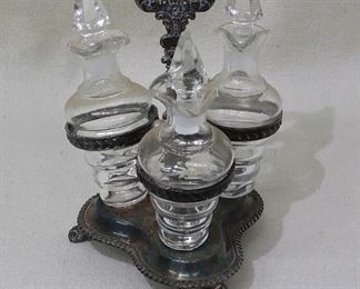 $50 Cruet set: footed silver stand w/ carrying handle, 3 glass cruets w/ glass stoppers.  Needs polishing! W: 5.5" | H: 8" | bottles: 5.5"   [Bin 34] 