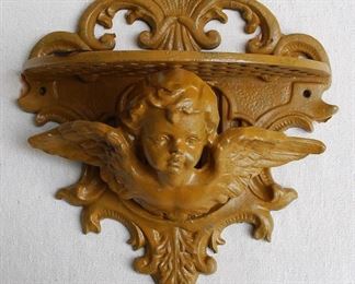 $60 - Wall shelf of cast metal painted dark ochre, winged cherub holding up shelf, scalloped back.  W: 10" | H: 11" | D: 5.5" [Bin 37]