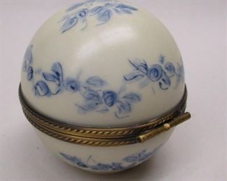 A ball shaped porcelain trinket box with hinged lid; when opened, an attached mini tea set is inside