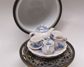 A ball shaped porcelain trinket box with hinged lid; when opened, an attached mini tea set is inside.  2.25" diameter.