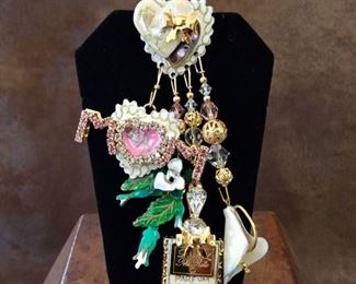 Lunch at the Ritz collectible designer pendant/brooch featuring hearts, flowers, Mom, and perfume. Size 2 1/8" x 3 3/4" high. Enameled components with rhinestone accents. Signed Lunch at the Ritz TM on back of heart at top and on perfume bottle. $120