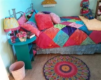 Colorful bed linens, rug, table, pillows, and handmade cloth doll. Queen mattress set with metal bed frame.