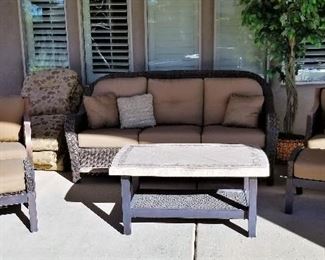 Outdoor wicker patio set. There are 2 side chairs with ottomans and a stone top coffee table.