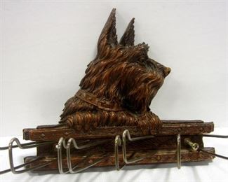 A vintage wall mount tie holder.  Made of syroco "wood" type material.  has eight movable metal bars.  Plaque has a relief image of a Scottie dog seated on an arm chair. Accented with gold paint.  Plaque is 6.75" tall
