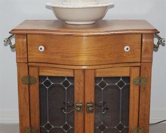 Pulaski Furniture Company Keepsake Collection Golden Oak Wash Stand with Brass Rod Towel Bars on each end,  Leaded Stain Glass Double Doors (30”W x 20”D x 28”H) shown with an Opalescent Glazed Ceramic Large Pitcher and Bowl Set. 