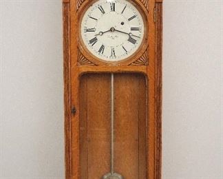 A late 19th century E. Howard & Co. Model 58 wall clock. 8-day weight driven time only movement marked "E. Howard & Co. Boston, 5" with 8 1/2" painted metal dial and Roman numerals marked "E. Howard & Co. Boston", round wooden pendulum rod with silver paint and damascened bob. Oak case with shaped top and turned finials over a single long door with circular upper glass and shaped lower, shaped lower drop with turned finials. Older refinishing with minor wear, several small paint flakes on dial, running when cataloged. 37 1/2" high overall. ESTIMATE $2,000-3,000