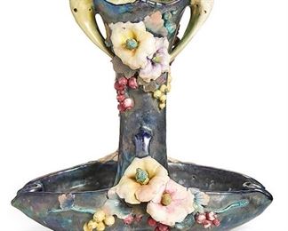 2020
An Amphora Double Centerpiece
Circa 1905-1910; Teplitz, Austria
Marked to base for: Amphora Works Turn-Teplitz and Amphora Riessner & Kessel: [Crown] / 830 / 58
The double-handled dark purple vessel with applied flowers and berries
14.75" H x 15" W x 9.5" D
Estimate: $400 - $600