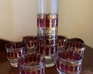 Liquor dispenser with six matching glasses. Set is red trimmed with gold design. 
