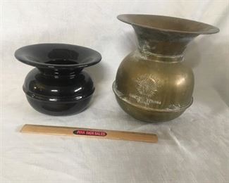 Cuspidors. The black one is ceramic and the other is brass. The brass one is weighted to keep it upright. The black one has some small chips in the finish.