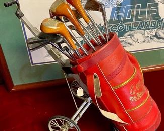 Lot 5141. $75.00. History of Golf Framed Art. Hand Signed C. Burton 1988. Signed and Numbered,  #944/1000. AND Novelty MINIATURE Golf clubs and Cart w/steel shafts Including 4 woods, Irons, Sand wedge and putter and a bag on wheels. Balls too.  Scotch Whisky or Old Andrews label on the bag.  Nice addition to your man cave!