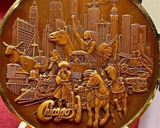 Lot 5145. $80.00. Very Cool Chicago Lot. T. Chamness Landmark Ink Art (18.5" H  x 14.25" W  has a plexiglass front, probably needs a piece of glass in there). A Wooden Medallion of Chicago Landmarks by Kurt Mager (6.25"dia).  A City of Chicago Crest clock with a hinge to reveal a clock (3"). The Medallion Plate by Pickard w/metal art by Kurt Mager (same art as the wooden medallion. 