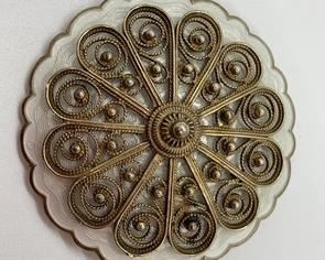 Lovely Norwegian sterling filigree piece in pristine condition. Delicate and ornate strands of sterling a curling pattern surround round silver beads, all mounted atop the white enamel surface of the brooch. The pin and clasp work well. Dimensions: 1-5/8" diameter. Wt. 21.3 gm. Marked with "925 S Sterling, Norway", and the Holth hallmark.