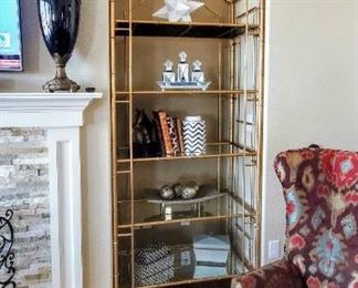 Black urn. Gold-tone open shelf. Household decorative items. Bold print wingback chairs.