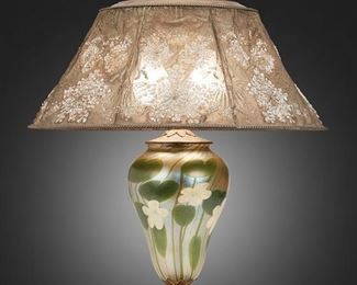 1
A Tiffany Studios Favrile Glass Table Lamp
Circa 1919-1928; New York, NY
Shade signed: Louis C. Tiffany Furnaces, Inc. / [L.C.T. monogram] / Favrile / 903 / Pat. Appd. For; Base signed: Louis C. Tiffany Furnaces, Inc. / [L.C.T. monogram] Favrile / 81 A
The enameled metal mesh shade with embossed Queen Anne's lace motif, green enameling to interior, white enameling to exterior, brass rope-style borders, and art glass finial on a two-light Favrile glass base with flower and stem motifs raised on a gilt-bronze foot with stylized foliate designs and inset enameled details, electrified
Overall: 23" H x 18" Dia.
Estimate: $3,000 - $5,000