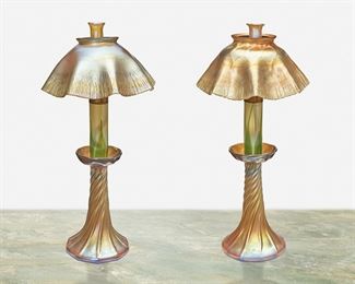 8
A Near-Pair Of L.C. Tiffany Favrile Glass Candle Lamps
Circa 1892-1919; New York, NY
Each signed: L.C.T.; One base with partial L.C.T. monogram paper label
Each gold iridescent Favrile glass with swirled base terminating in a bobeche issuing a glass candle holder with green pulled feather motif fitted with a metal knob to control the wick and topped with a scalloped onion skin shade, 2 pieces
Each: 14.5" H x 7.25" Dia.
Estimate: $3,000 - $5,000