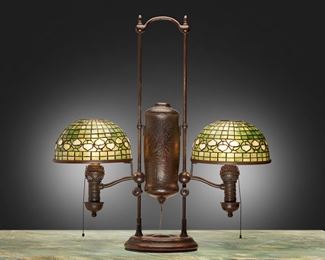 26
A Tiffany Studios Double-Arm Student Lamp
1901; New York, NY
One shade signed: Tiffany Studios / New York; Base marked: 21346
The two green and white leaded glass "Acorn" shades on an etched and patinated bronze Hartshorn converted oil lamp base with Manhattan Brass Co. spiral tubes decorated with low relief floral motif, electrified
Overall: 29.25" H x 27.5" W x 10.25" D; Each shade: 10" Dia.
Estimate: $8,000 - $10,000
