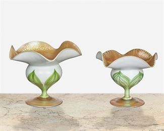 43
Two L.C. Tiffany Favrile Glass Floriform Cabinet Vases
1909 and 1918; New York, NY
First signed: L.C. Tiffany / Favrile / 5366 D; Second signed: L.C. Tiffany / Favrile / 1529-1261 M
Each bulbous floriform vase with wide ruffled edge, gold iridescent onion skin interior, and white glass exterior with green pulled feathers atop blue iridescent bases, 2 pieces
Larger: 5" H x 5.75" Dia.
Estimate: $800 - $1,200