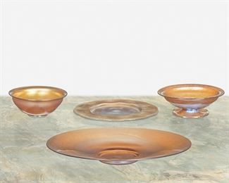 69
Four L.C. Tiffany Favrile Glass Items
Late 19th/early 20th Century; New York, NY
Footed plate signed: L.C. Tiffany / Favrile; Plate signed: L.C. Tiffany / Favrile / 1877; Dish signed: L.C.T.; Bowl signed: L.C.T. / Favrile / 5
Each gold iridescent Favrile glass, comprising a large blue-shaded footed plate with onion skin, a medium onion skin plate with scalloped edge, a blue-shaded footed dish with optical base, and a small blue-shaded bowl, 4 pieces
Largest: 1.5" H x 12" Dia.; Smallest: 2" H x 5.25" Dia.
Estimate: $600 - $800