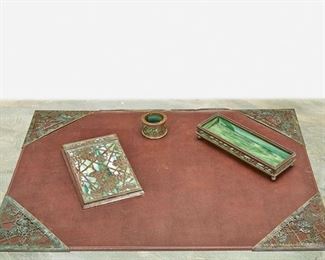 152
A Tiffany Studios "Grape And Vine" Desk Set
Circa 1902-1919; New York, NY
Each signed: Tiffany Studios / New York; Further marked: 903 / 981 / 997
Each patinated bronze with green mottled glass and "Grape Vine" motif overlay with areas of verdigris patination, comprising a memoranda pad with wood back, a pen tray, a pen wiper, and four blotter corners, 7 pieces
Largest: 7.75" H x 4.75" W x .75" D; Smallest: 1.5" H x 1.25" Dia.
Estimate: $800 - $1,200