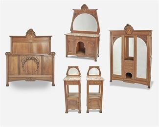 192
An Art Nouveau Walnut Marquetry Bedroom Set
Late 19th/early 20th Century
The walnut bedroom set with high relief carved floral details and marquetry portrait roundels with mother-of-pearl inlay, comprising a headboard (66.25" H x 57.5" W x 4" D) and footboard (39.5" H x 57" W x 1.75" D), a two-door mirrored armoire with two open central compartments and four drawers (90.5" H x 67" W x 23" D), a vanity with pink marble top over two drawers and two cupboards with open central compartment (76" H x 47.25" W x 19.75" D), and two side tables each with a mirror and pink marble top over a single drawer and undertray (Each: 43.5" H x 15.75" W x 15.75" D), 6 pieces
Estimate: $2,000 - $3,000
