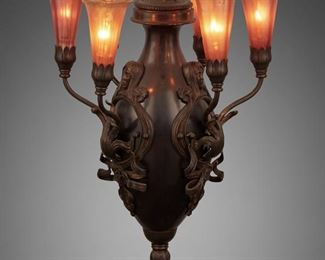 197
An Art Nouveau Bronze And Art Glass Chandelier
First-quarter 20th Century
The bronze chandelier with applied figural masks and scrolling foliate designs issuing six upright gold and pink iridescent glass tulip shades and fitted with associated patinated metal stem and canopy, electrified
43" H x 13" Dia.
Estimate: $1,000 - $1,500