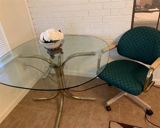 Glass top table on brass base with one rolling arm chair