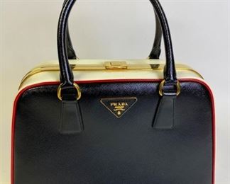 Lot	213	Prada Saffiano Lux Pyramid Two Tone Bag	Signature saffiano leather in black and contrasting white with red piping, gold tone hardware, Prada logo triangle at top center, push lock closure at top, blush pink leather lining with two zip pockets and two slip pockets, made in Italy. Dust bag included. Excellent condition. 13" L x 9" h x 5" D Appears rarely used if at all
