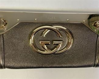 Lot	221	Gucci Pewter & Gold Interlocking GG Clutch	Gucci Pewter & Gold Leather Starlight Interlocking GG Logo Clutch. Pewter leather with pale gold metal frame and interlocking GG logo at front. Twist lock closures at each end. Leather lining with slip-in pocket. 9"l x 4.25"w x 1" d
