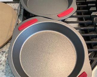 Lot 5555. $35.00 This lot features a "like new" 13" Pampered Chef pizza stone and two metal carrying racks; 2 Food Network Pie Pans and an 8" square metal dish.