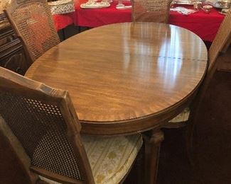 Mid-century dining table by White. Comes with 4 caned-back chairs. Measures 41” W x 60” L.  Has two 20” leaves. 