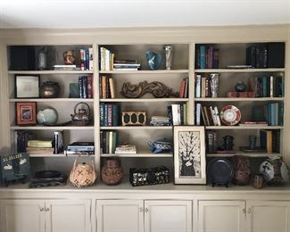 Cabinet shelves filled with antique and contemporary pottery, books and art.
