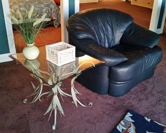 One of two navy blue leather chairs and a glass top end table, which is part of a three-piece set