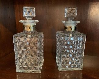 $50 - Pair of vintage glass decanters; one "Scotch" and one "Rye." Each with stoppers; some chips and wear to each stopper. 9 in. tall x 3 1/2 in. square bottle.
