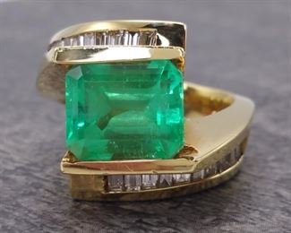 Before now very few have seen the color of tropical sea green like that similar to Emeralds from Columbia. This special ~5 ctw Columbian Emerald Cut Emerald is one such gem. The Emerald is set on the long side and nestled between 2.20 Carats of intensely bright channel set diamond baguettes and artfully molded into a modernistic and sophisticated look with 18k Yellow Gold. You may see something similar but never...never see this color and style again.