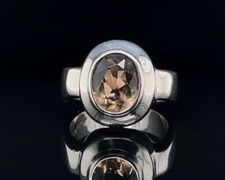 A vivacious champagne colored bezel set 2.20 carat oval cut Smoky Quartz is set in mid century modern style amidst quality sterling silver. An Impressionable ring.