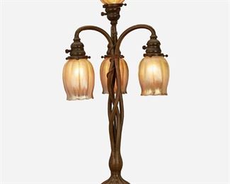 8
A Tiffany Studios Patinated Bronze Table Lamp
Circa 1899-1900; New York, NY
Each shade signed: L.C.T.; Base signed: Tiffany Studios / New York / S 1129 / 1
The patinated bronze table lamp with an intertwined vine-style base with a pinched and fluted foot issuing three drop pendant lights and one central light, each with gold iridescent Favrile glass floriform shades, electrified
Overall: 30.25" H x 9.5" Dia.
Estimate: $1,000 - $2,000