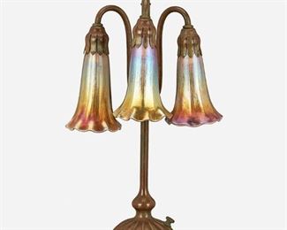 7
A Tiffany Studios Three-Light Lily Table Lamp
Circa 1902-1919; New York, NY
Each shade signed: L.C.T. / Favrile; Base signed: Tiffany Studios / New York / 306
The verdigris patinated bronze base with a domed ribbed foot and slender stem issuing a drop cluster of three gold iridescent Favrile glass "Blossom" shades, electrified
16" H x 8" W x 8.5" D
Estimate: $1,200 - $1,800