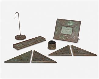 21
A Group Of Tiffany Studios "Pine Needle" Desk Set Items
Circa 1902-1919; New York, NY
Each signed: Tiffany Studios / New York; Further marked: 940 / 961 / 981 / 997 / 1004
Each mottled green glass with patinated bronze pine needle motif overlay, comprising a calendar frame, a pen tray, a bill file hook, four bronze blotter corners, and a pen brush, 8 pieces
Largest: 6.5" H x 7.5" W x 3.125" D; Smallest: 2" H x 2.25" Dia.
Estimate: $500 - $700